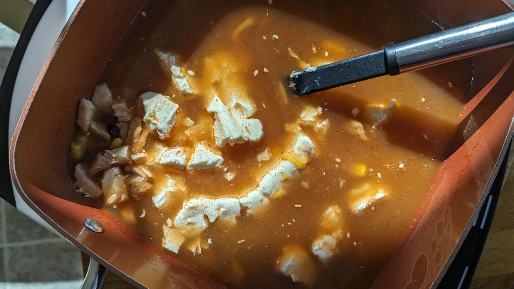 Adding the cheeses to the pot to make Creamy Chicken Enchilada Soup