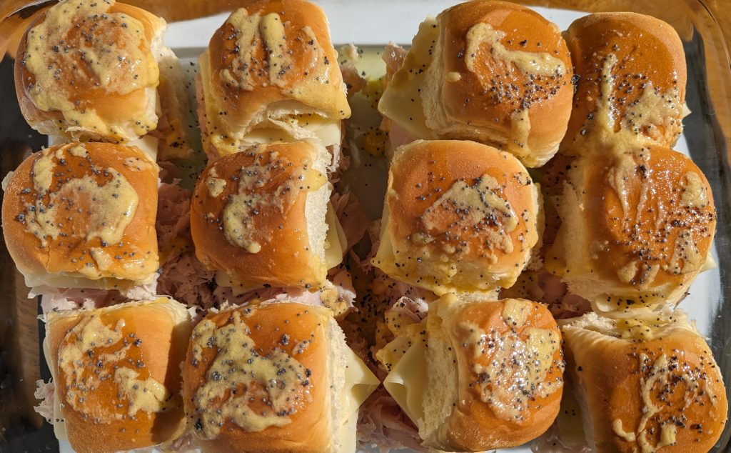 Ham and swiss cheese sliders with marinade and poppy seeds on top.