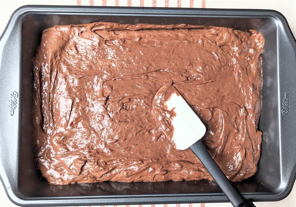 chocolate covered cherry cake batter being spreadd in pan with a spatula