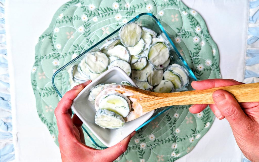 cucumber sour cream salad being put into serving bowl