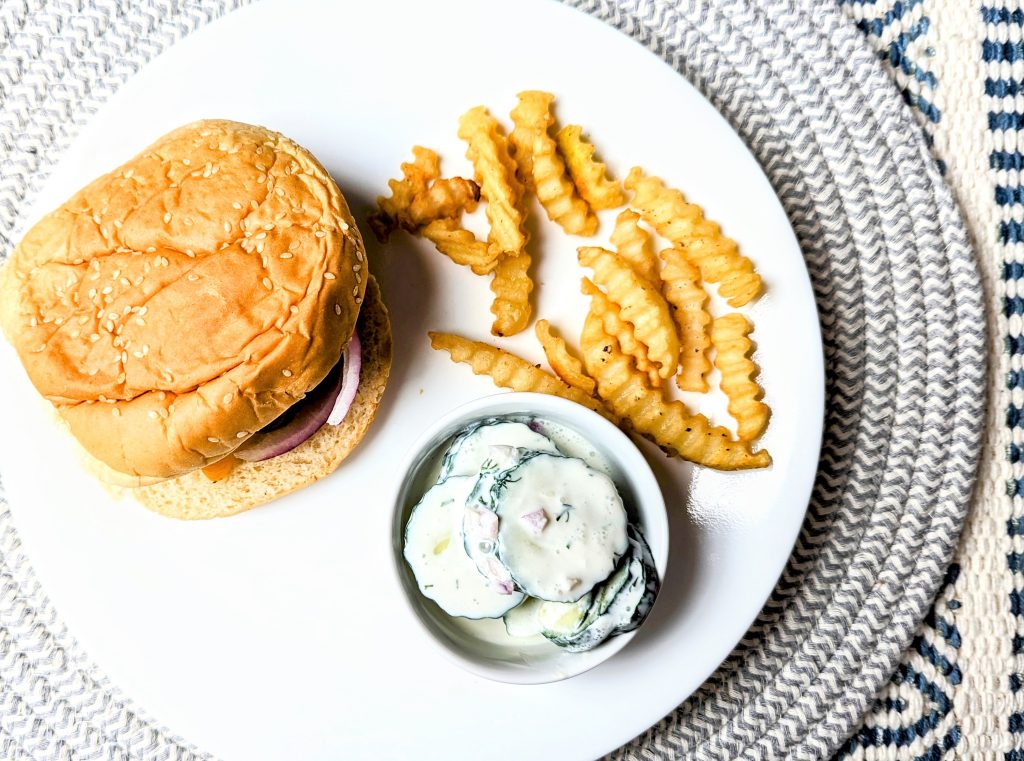 cucumber sour cream salad on plate with burger and fries