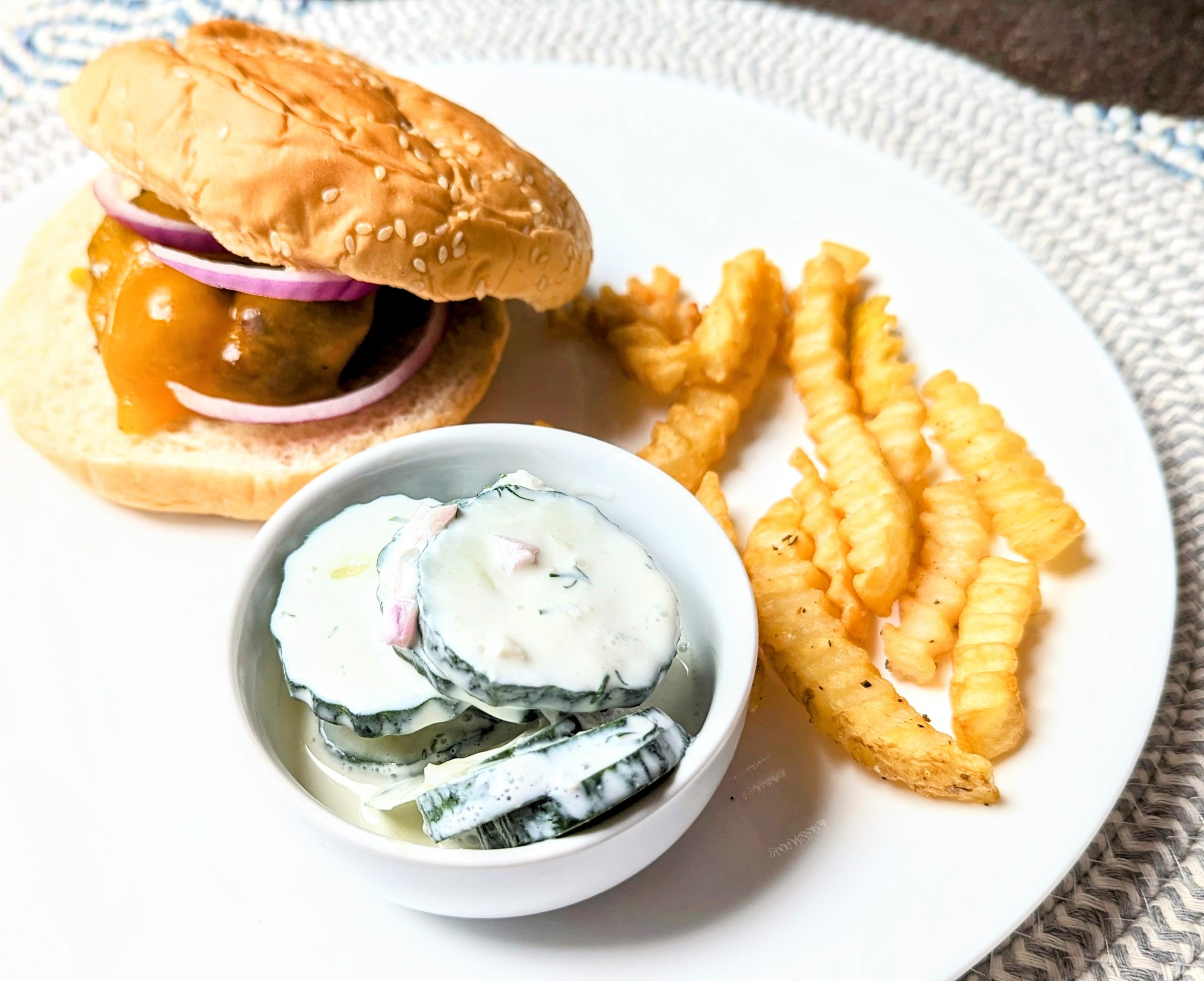 cucumber sour cream salad on plate with burger and fries