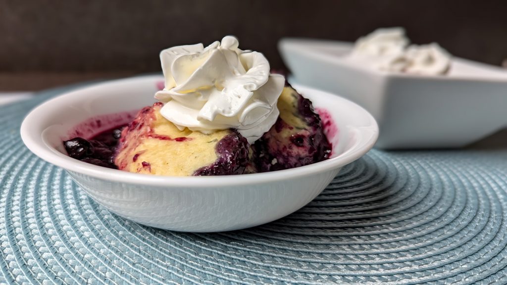 stovetop blueberry grunt in serving bowl with whipped cream