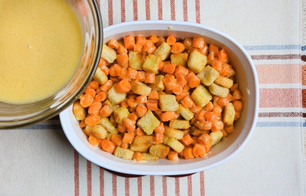 pouring sauce onto creamy cheesy carrot casserole