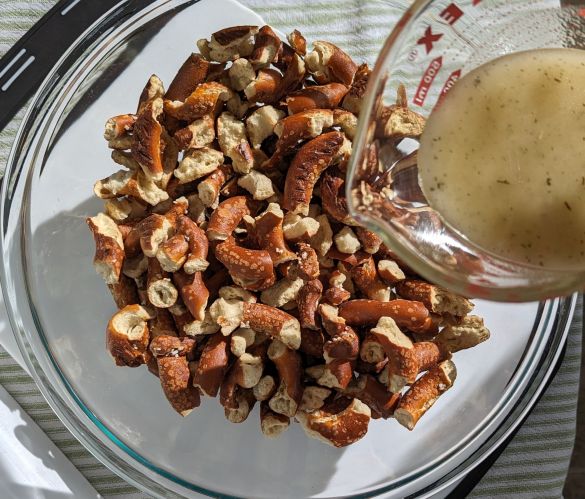 pouring oil mixture over pretzels in bowl