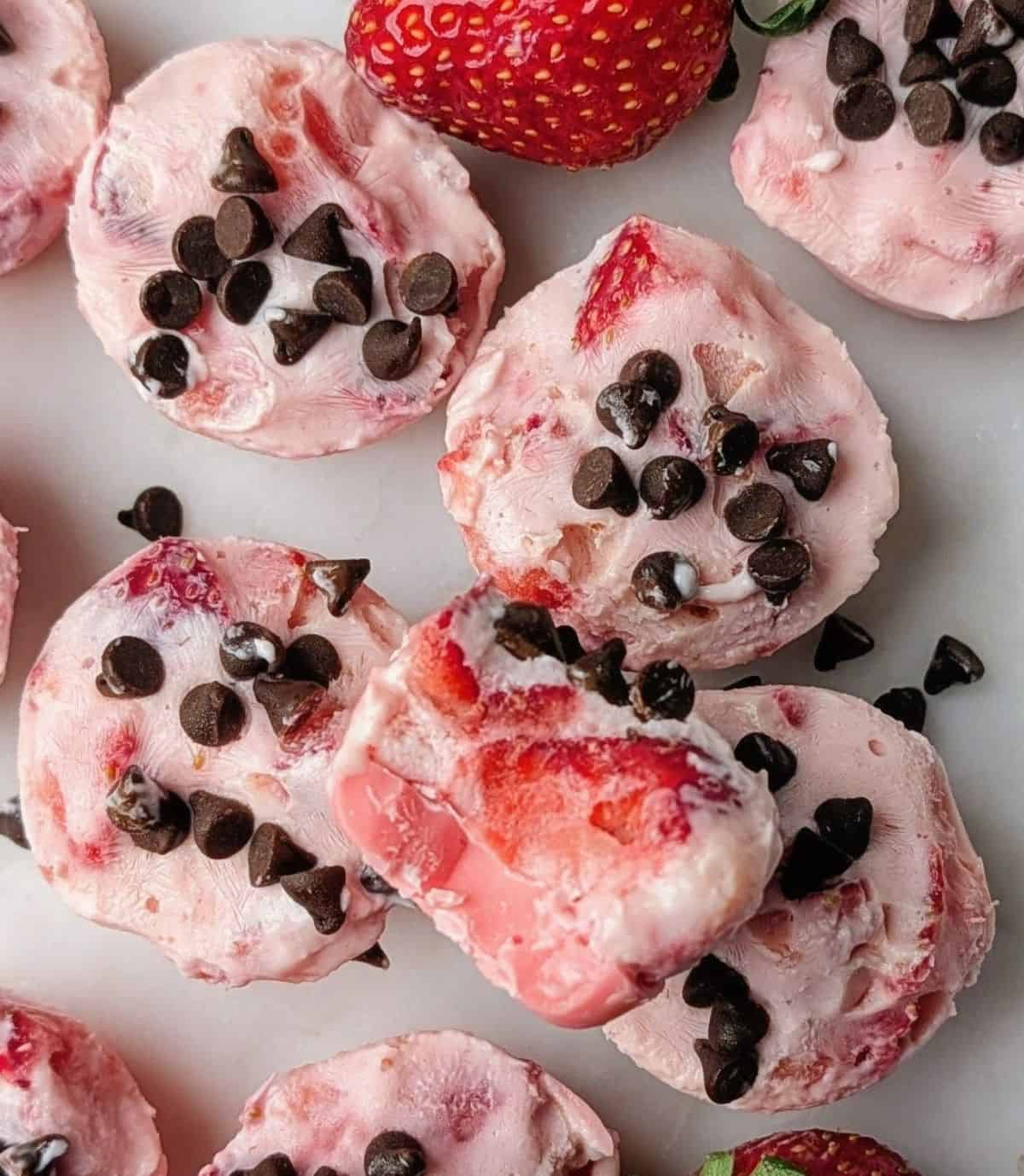 Close up of a frozen strawberry yogurt bite with a pink candy base and creamy Greek yogurt filling.