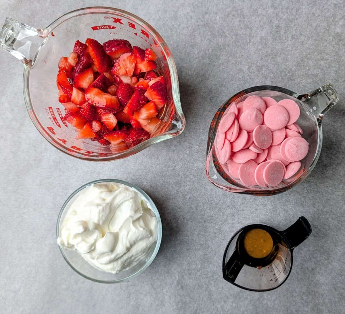 Ingredients for frozen strawberry yogurt bites including pink candy melts, Greek yogurt, fresh strawberries, and honey.