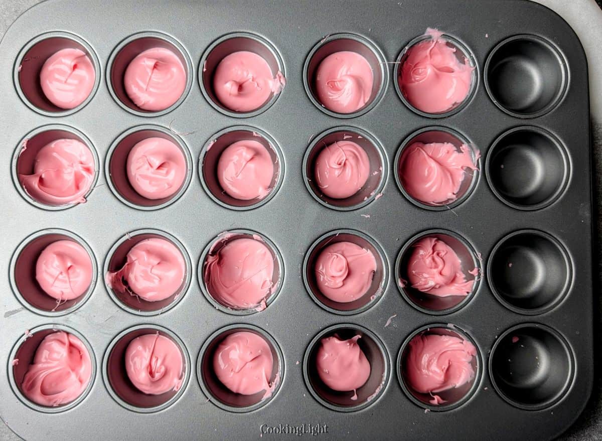 Melted pink candy wafers being poured into a mini muffin pan for the yogurt bite base.