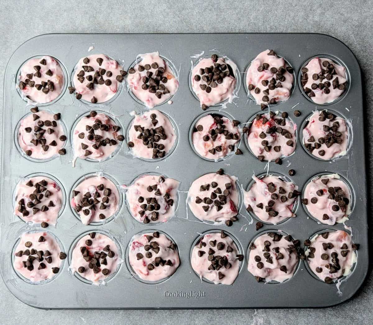 A tray of finished frozen strawberry yogurt bites topped with mini chocolate chips.