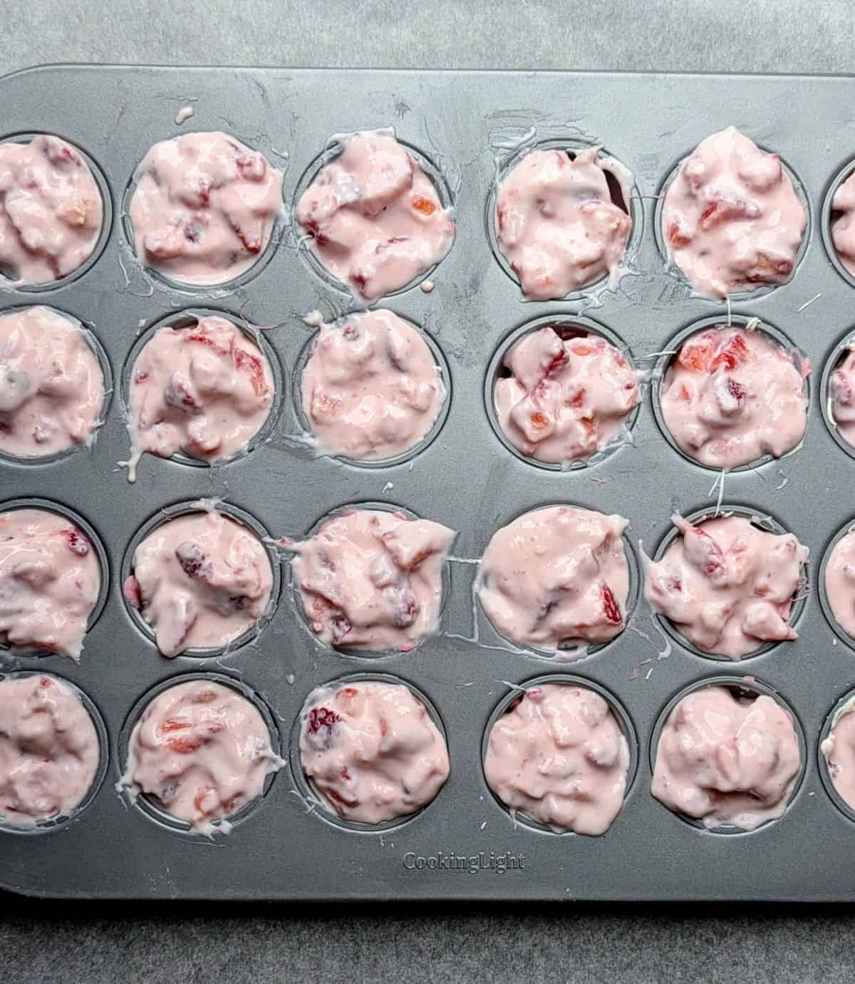 Spoonfuls of Greek yogurt and fresh strawberry mixture being added on top of pink candy cups.