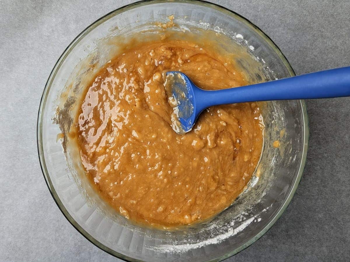 Using a blue spatula to stir the flour mixture into the wet ingredients for Valentine cookie bars in a glass bowl.