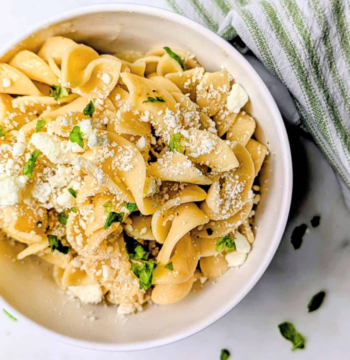 Bowl of buttered egg noodles with crumbled feta cheese and basil