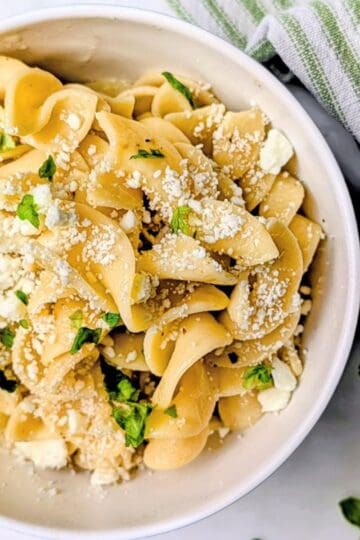 Bowl of buttered egg noodles with crumbled feta cheese and basil