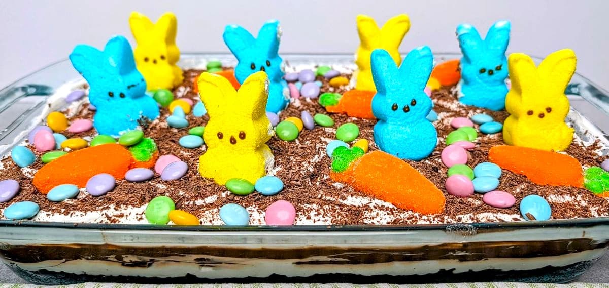 A finished Easter chocolate lasagna in a glass pan topped with yellow, blue, and orange marshmallow Peeps and chocolate shavings.