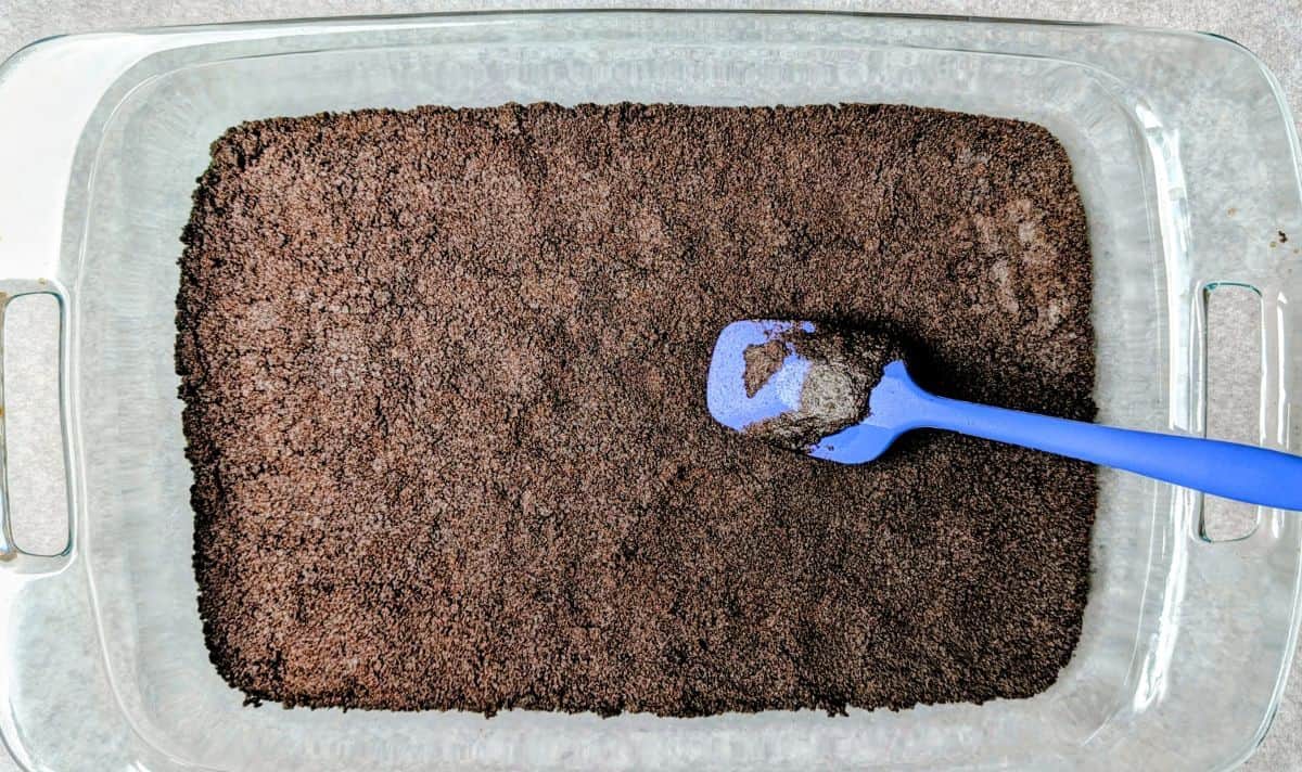 Pressing the crushed Oreo and butter crust into a glass baking dish for chocolate lasagna.