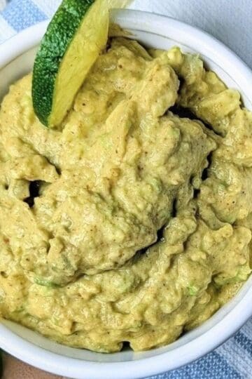 Healthy guacamole recipe in a white bowl with lime garnish.