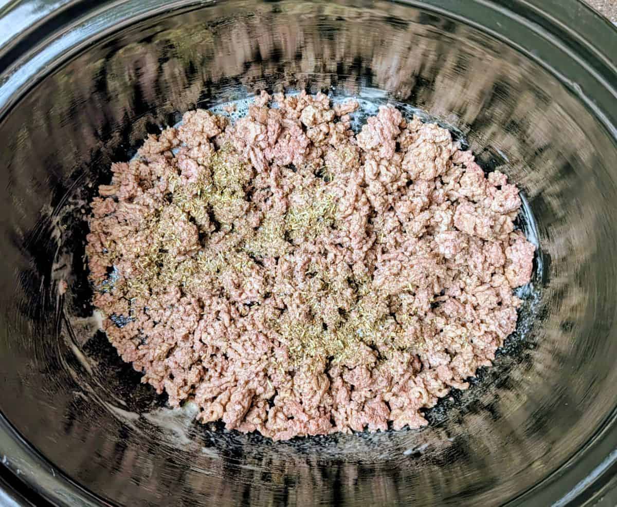 Browned ground beef mixed with Italian seasonings in a slow cooker for an Olive Garden pasta fagioli recipe.