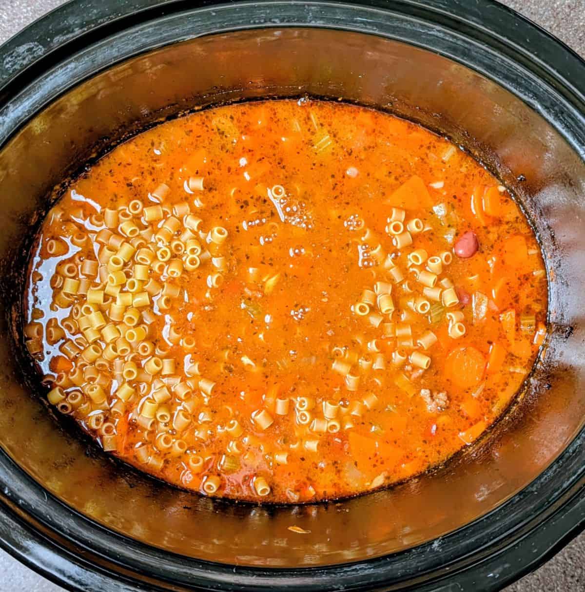 Adding uncooked ditalini pasta to the slow cooker for the final step of the Olive Garden pasta fagioli recipe.