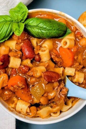A white bowl of Olive Garden slow cooker pasta fagioli soup topped with fresh basil and served with a blue spoon.
