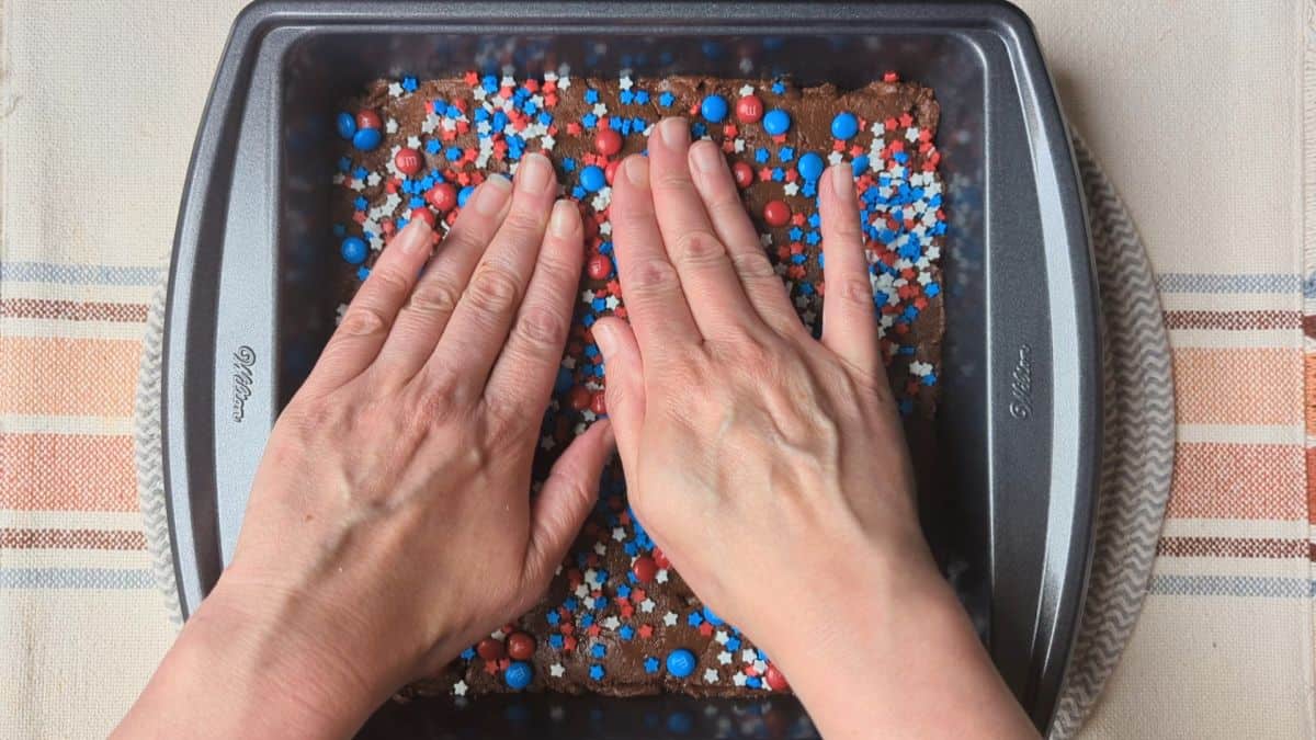 Pressing red, white, and blue star-shaped candies into a smooth layer of melted chocolate to decorate the fudge.