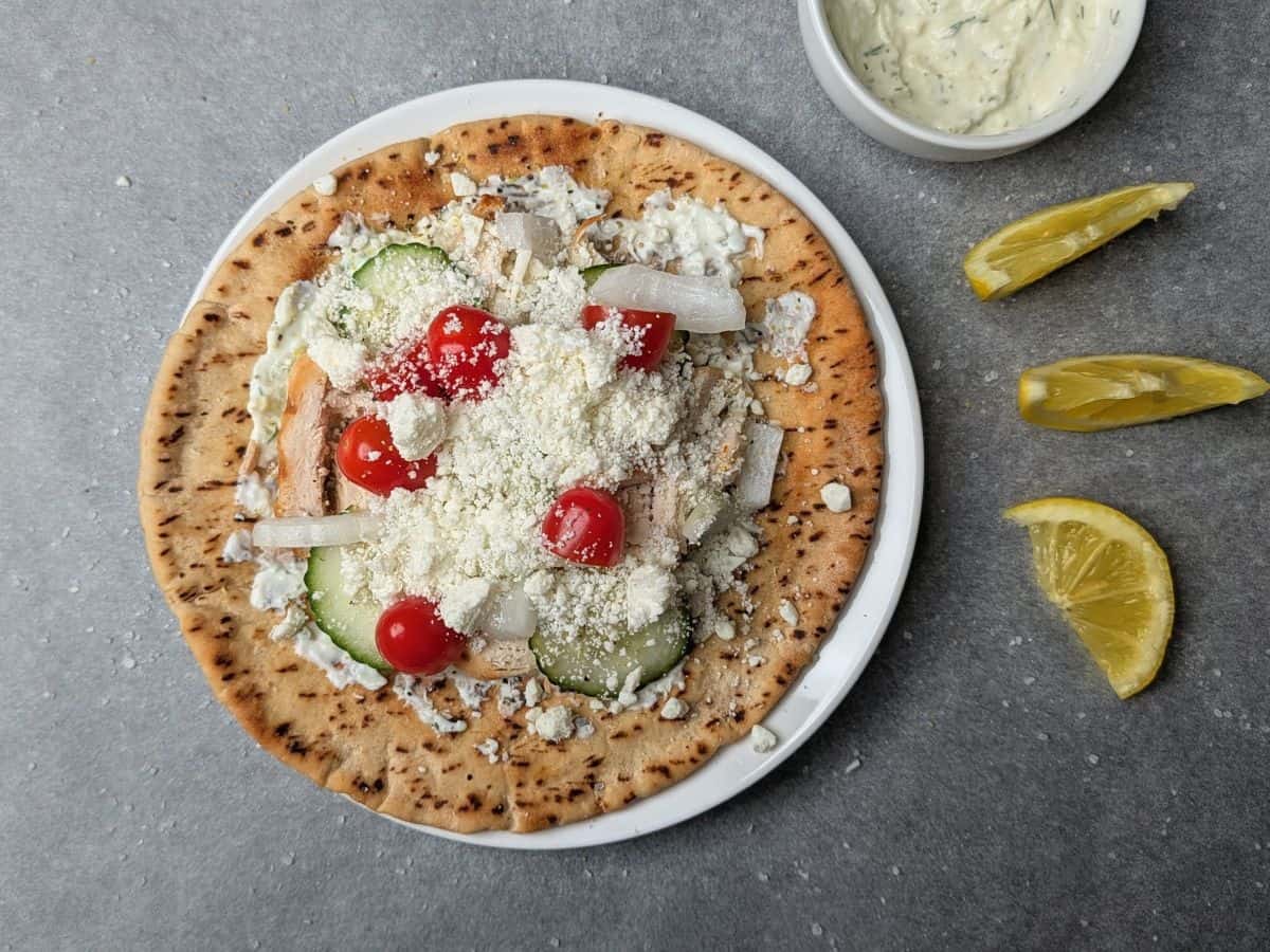 A fresh homemade chicken gyro topped with sliced cucumbers, cherry tomatoes, and red onions on a warm pita bread. feta added.