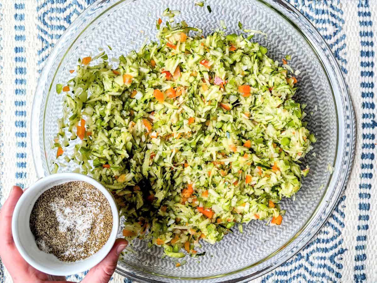 Homemade zucchini coleslaw recipe featuring freshly grated zucchini and finely diced red peppers in a glass mixing bowl