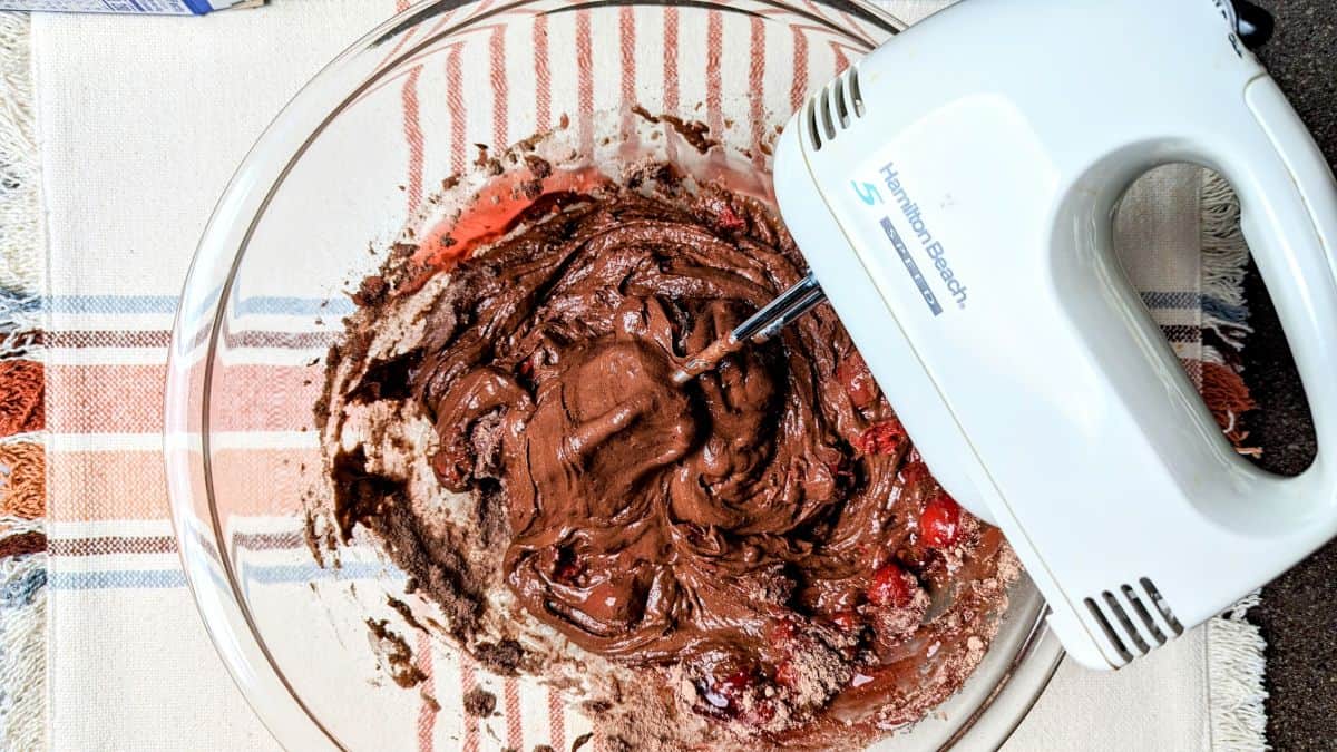 Mixing the chocolate covered cherry cake batter in a white bowl using a hand mixer to combine the cake mix and cherry pie filling.