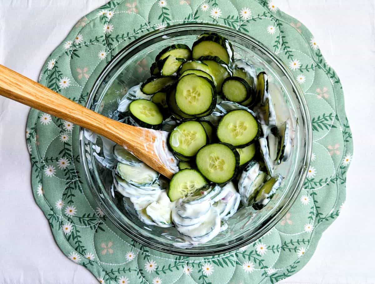 Thinly sliced English cucumbers being tossed into a bowl of creamy sour cream and dill dressing.