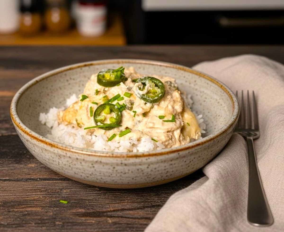 A white bowl filled with creamy jalapeño popper chicken topped with fresh sliced jalapeños and melted cheese, served on a gray napkin.