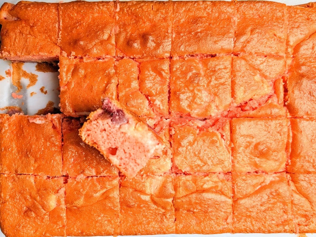 A top-down view of a freshly baked strawberry earthquake cake in a rectangular baking pan, sliced into even squares.