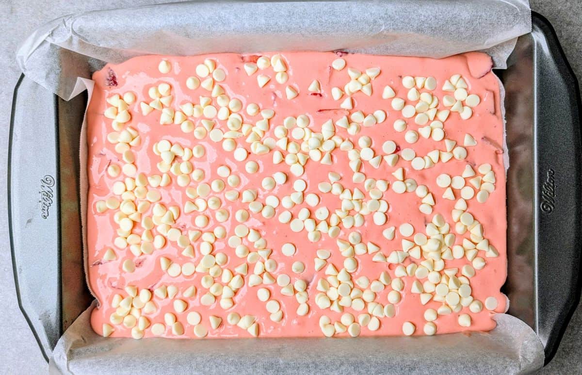 A rectangular baking pan filled with strawberry earthquake cake batter, topped with a generous layer of white chocolate chips.