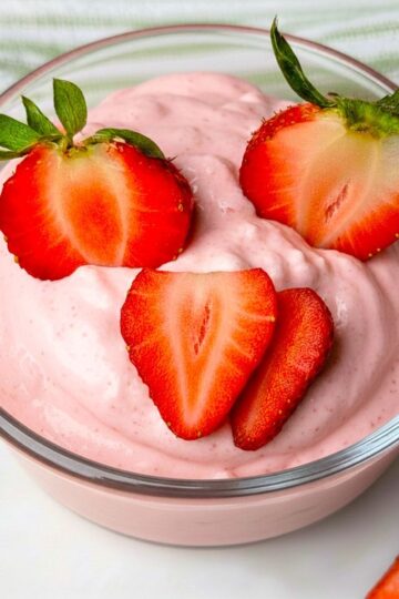A glass serving bowl filled with creamy pink strawberry fluff salad, topped with three fresh strawberry halves for garnish.