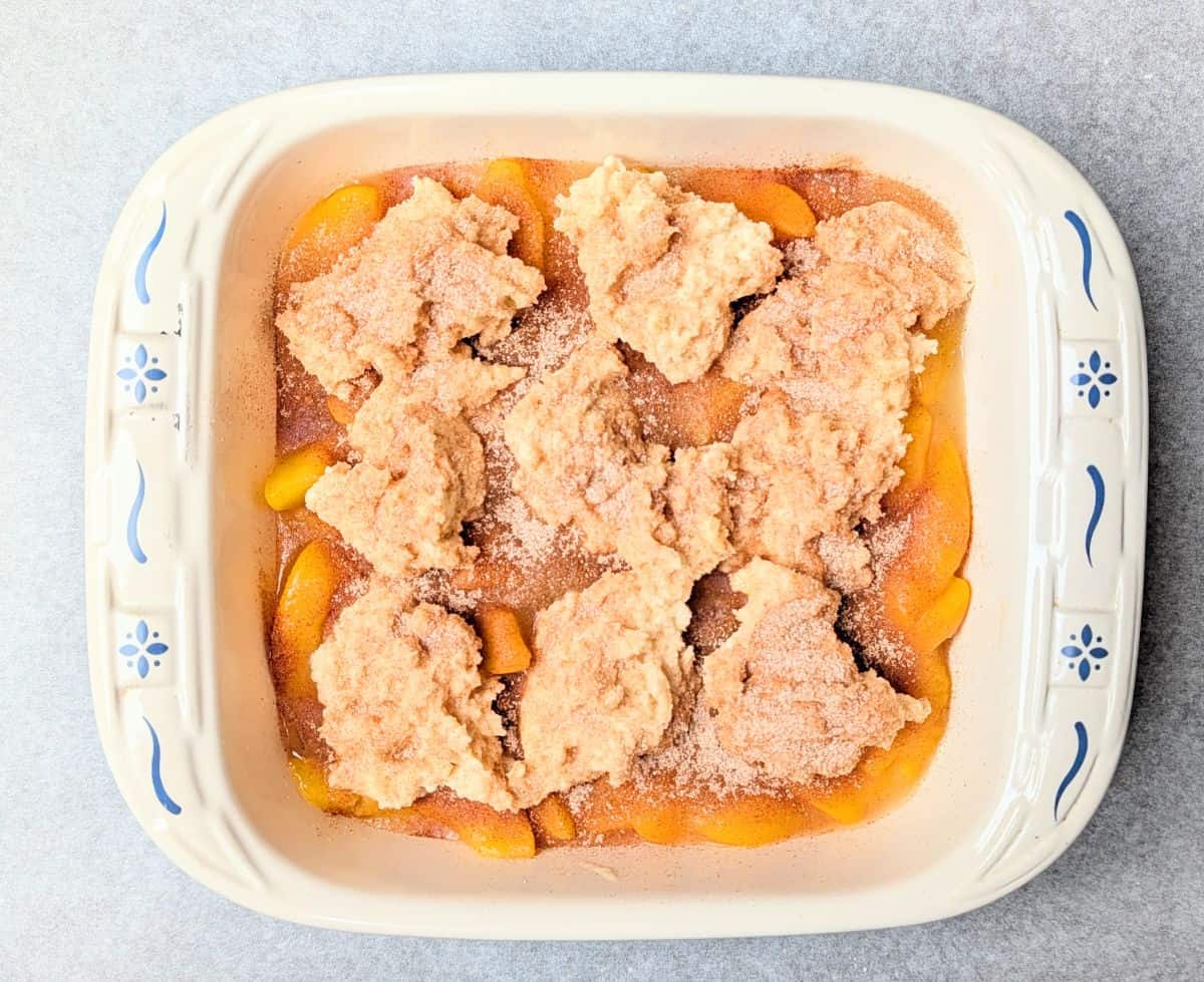 raw biscuit dough being added to top of peach cobbler in 9 spoonfuls