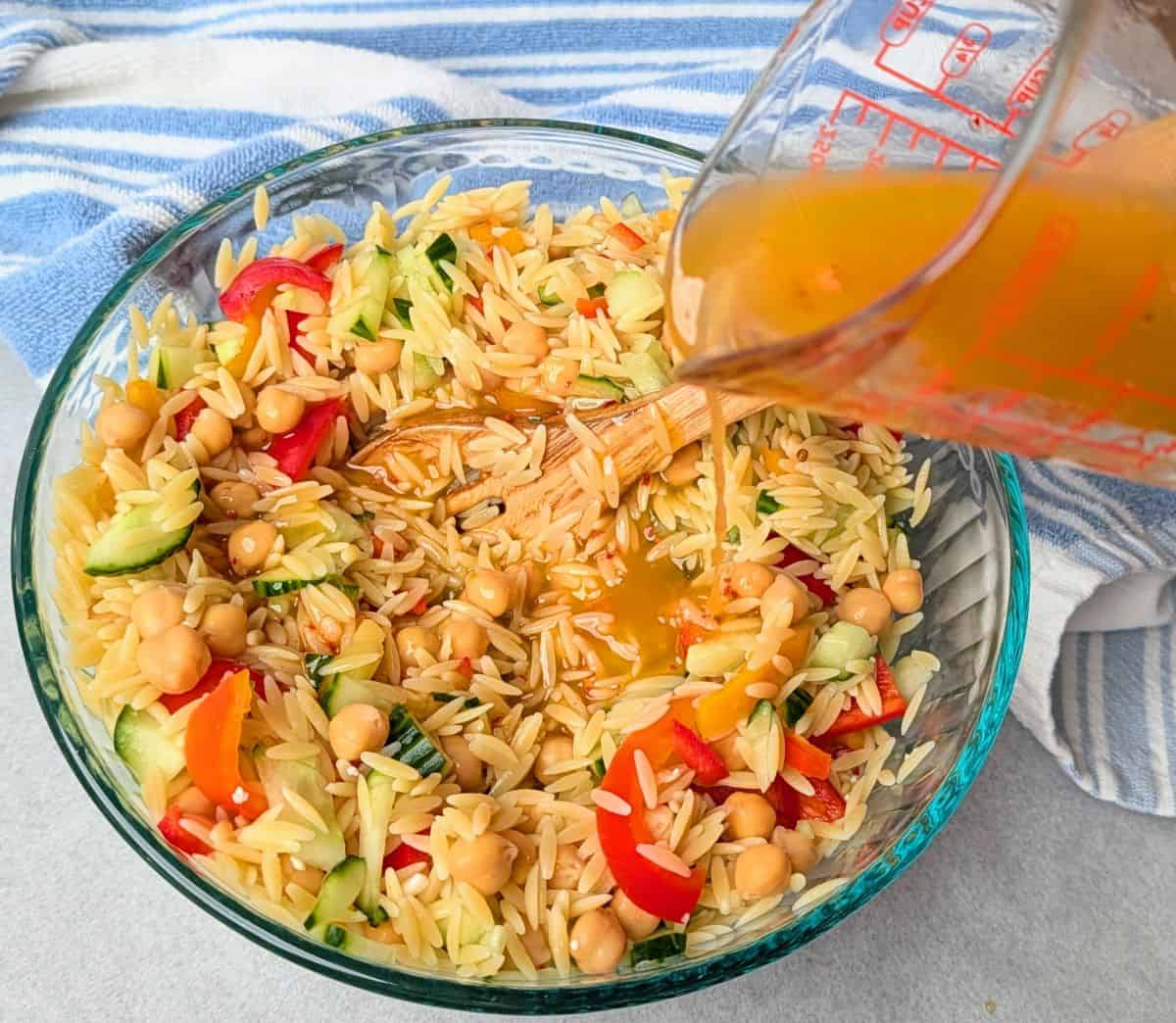 pouring mediterranean dressing over orzo salad
