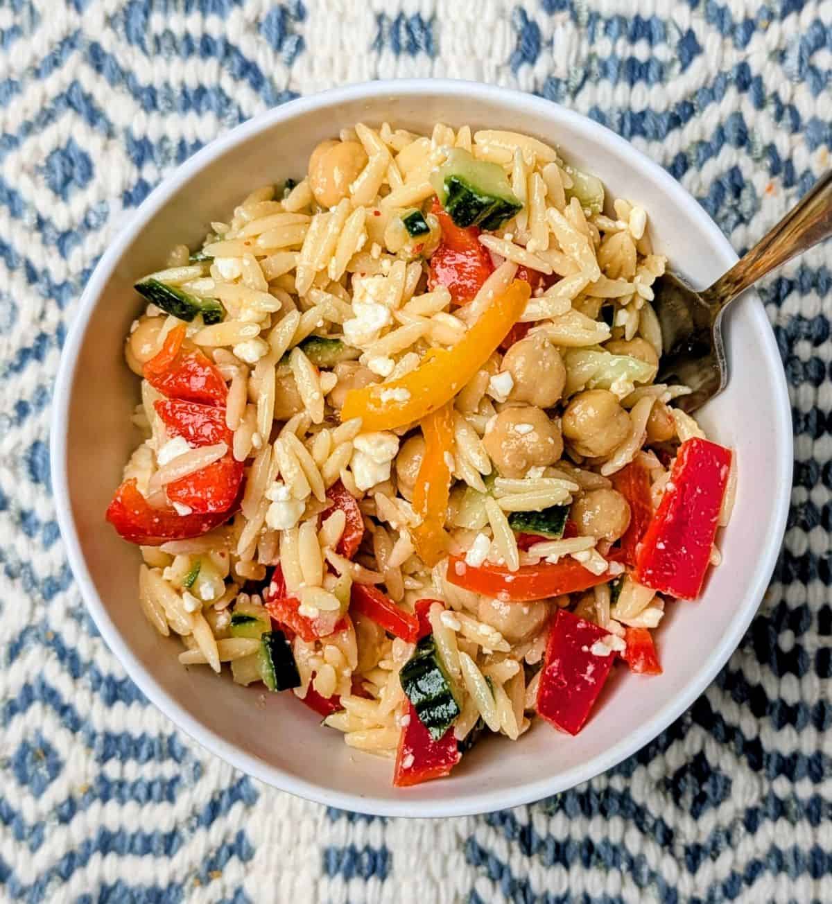 Overhead view of homemade Orzo Greek Salad mixed with fresh tomatoes, feta, and herbs in a white serving bowl with a silver fork.