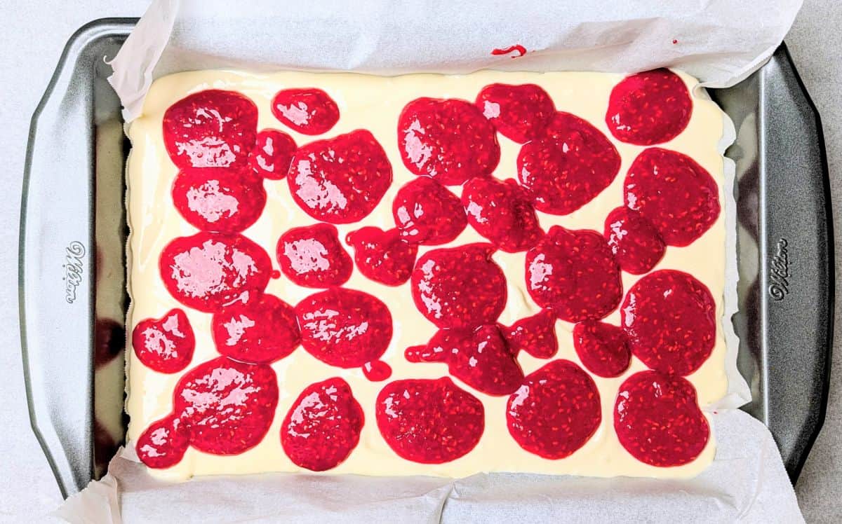 Dropping dollops of bright red raspberry puree onto the smooth filling for raspberry lemon cheesecake bars.