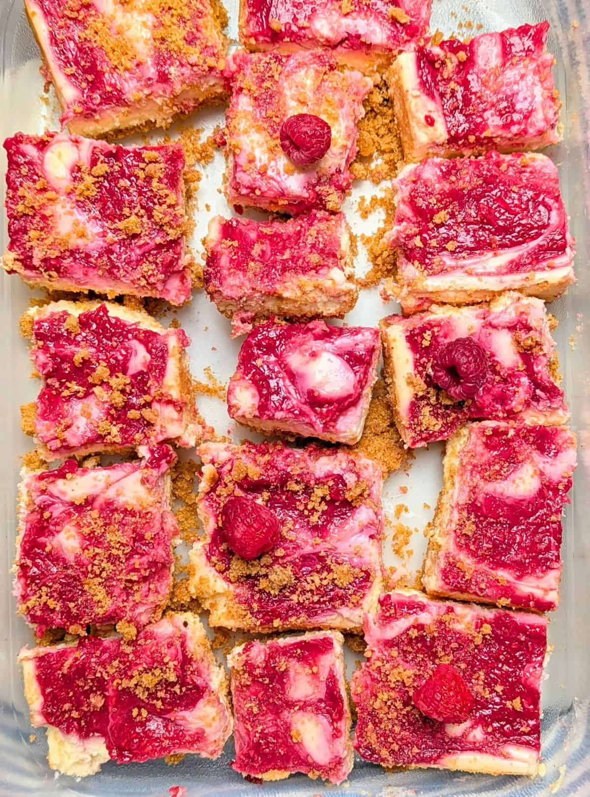 Sliced raspberry lemon cheesecake bars stored in a clear plastic container for easy transport.