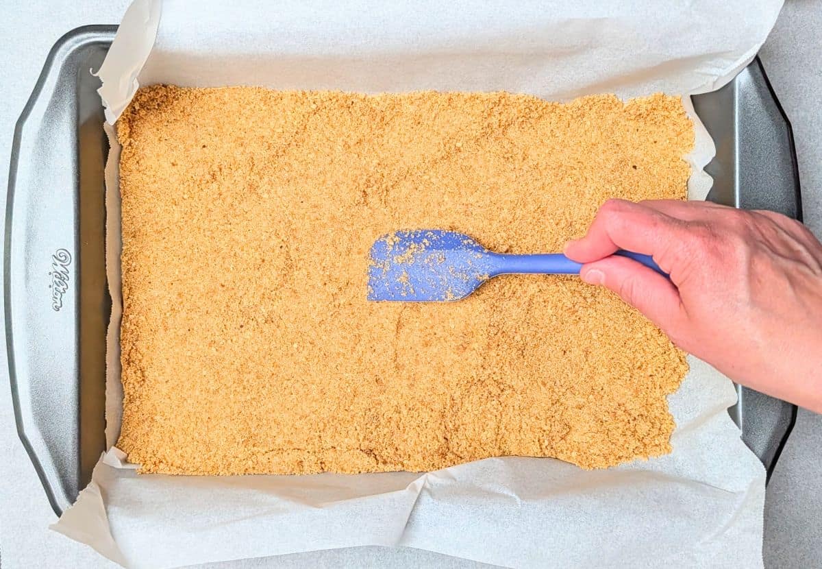 Spreading the buttery graham cracker crust into a baking dish for raspberry lemon cheesecake bars.