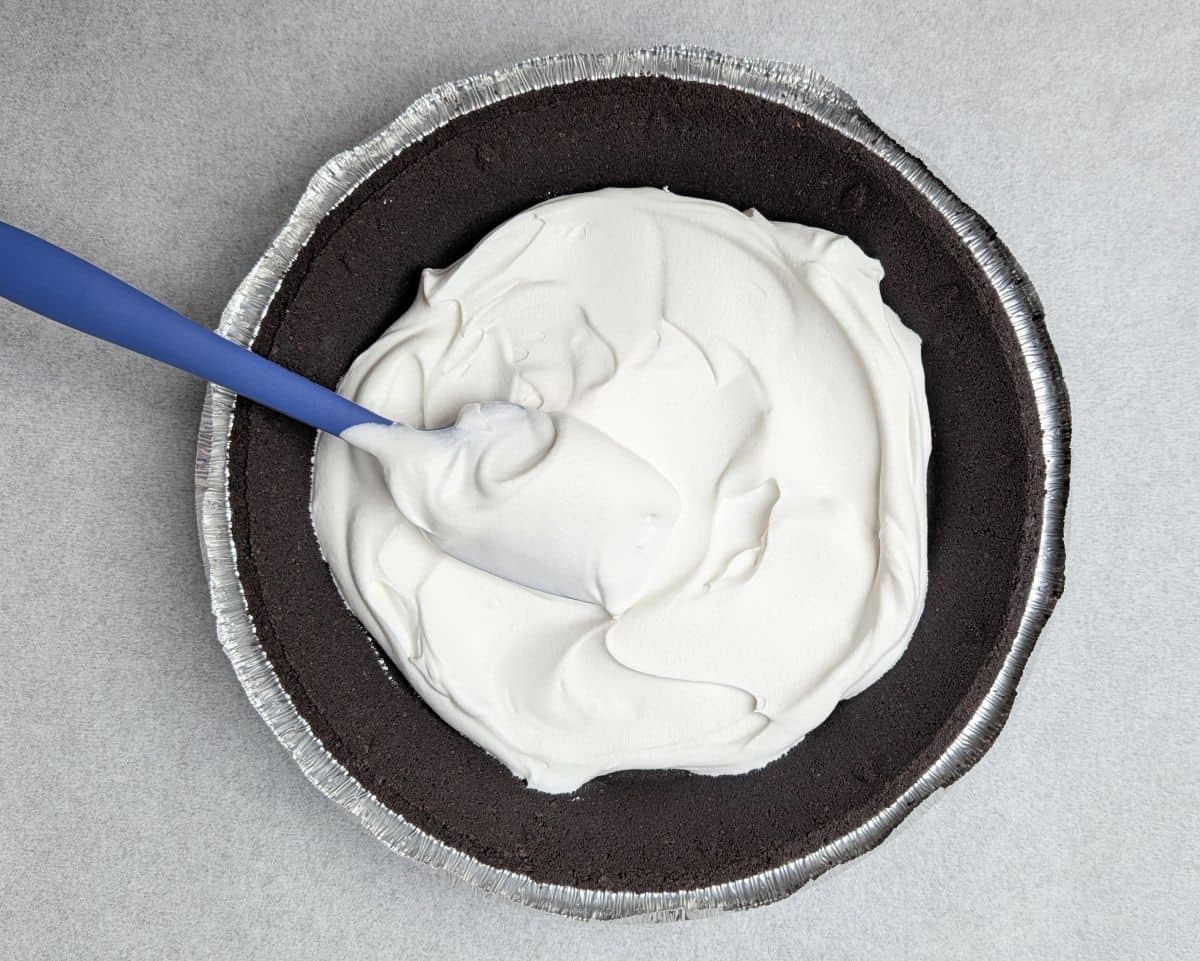 Spreading whipped cream over the chocolate crust of an easy Black Forest pie.