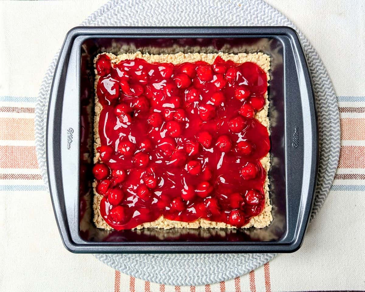 Cherry pie filling spread evenly over a crumb crust in a square baking pan.