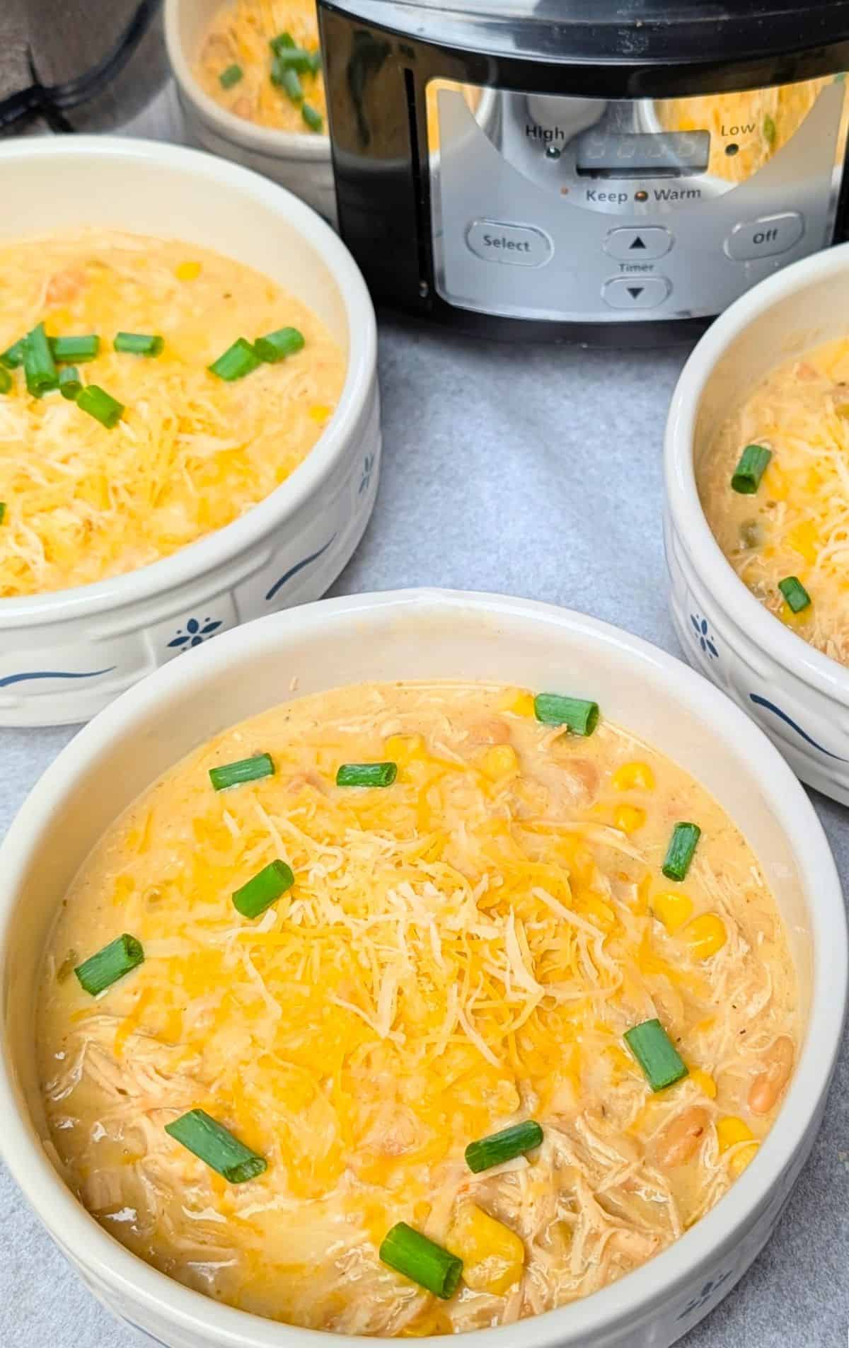 A top-down view of two white and blue patterned bowls filled with rich, creamy crockpot cream cheese chicken chili, garnished with corn.