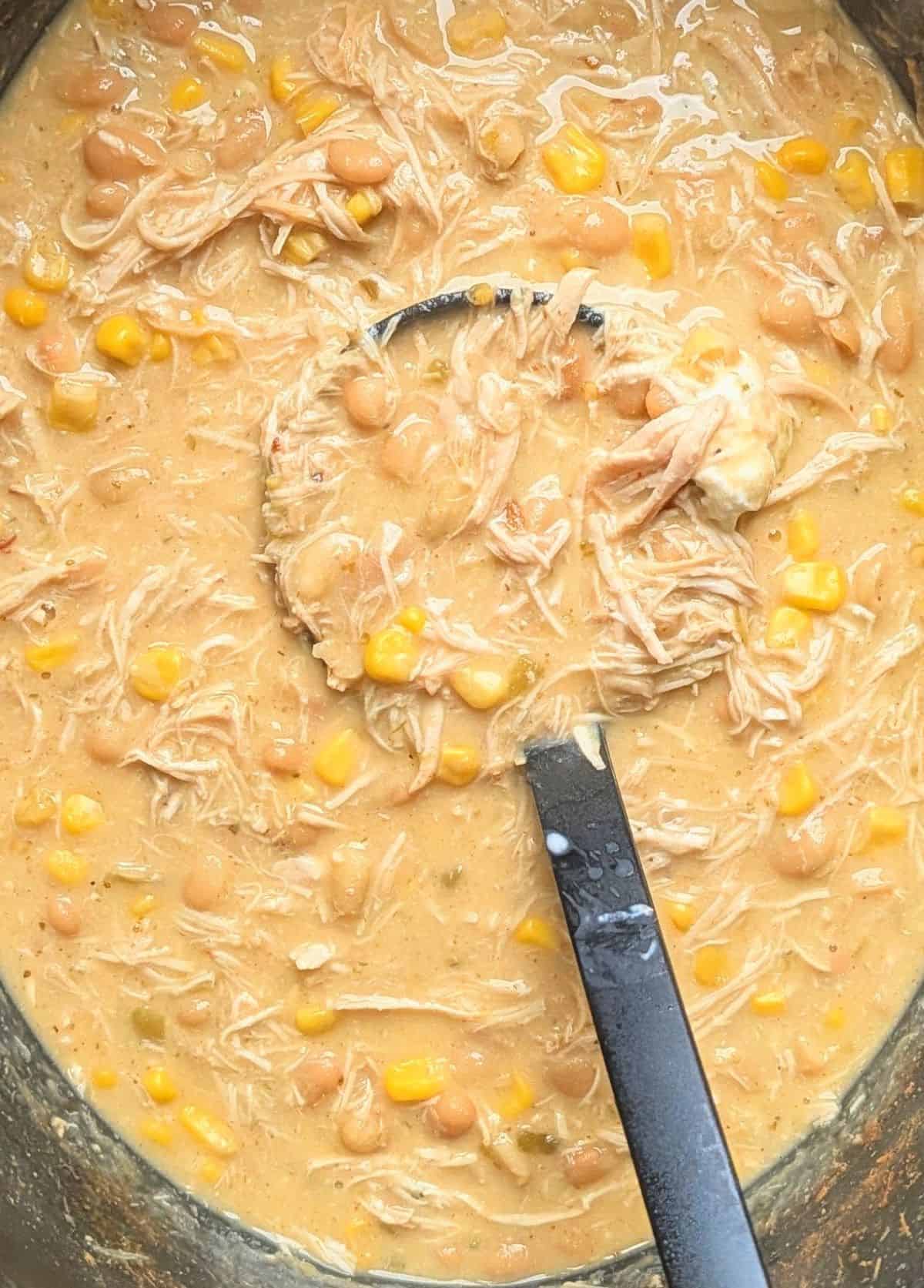 A ladle lifting a hearty scoop of cream cheese chicken chili from a crockpot.