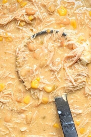 A close-up of a black ladle scooping thick, creamy crockpot cream cheese chicken chili, showing shredded chicken, corn, and beans right out of the slow cooker.