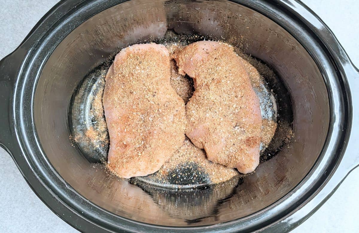 Seasoned raw chicken breasts inside a slow cooker ready to make crockpot cream cheese chicken chili.