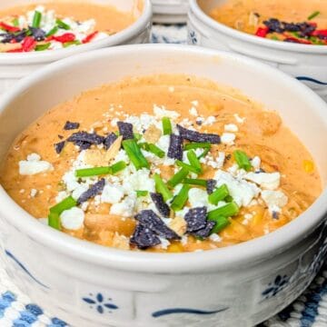 A close-up of a white and blue patterned bowl filled with creamy Mexican street corn soup, garnished with crumbled cheese, spices, and fresh herbs.