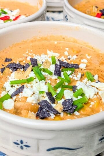 A close-up of a white and blue patterned bowl filled with creamy Mexican street corn soup, garnished with crumbled cheese, spices, and fresh herbs.