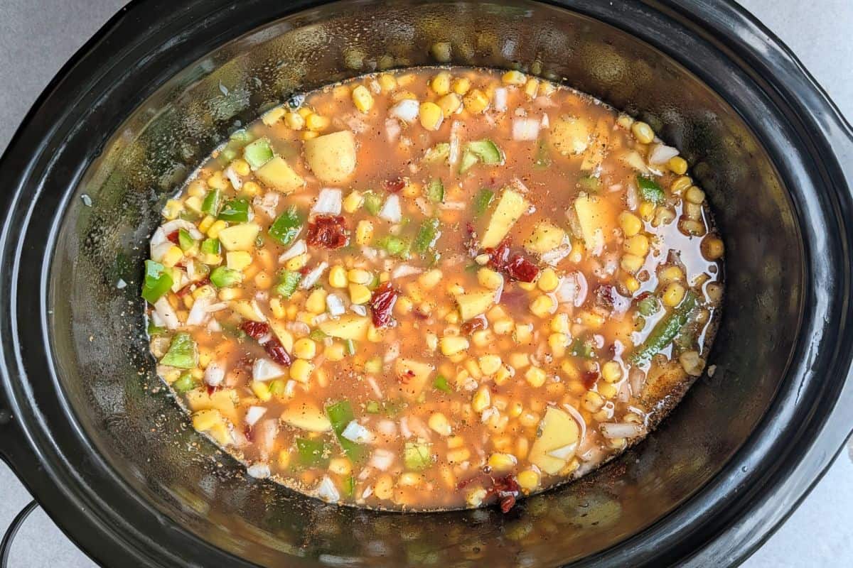 Adding chicken broth over fresh corn, potatoes, and seasonings in a crockpot to make an easy slow cooker corn chowder.
