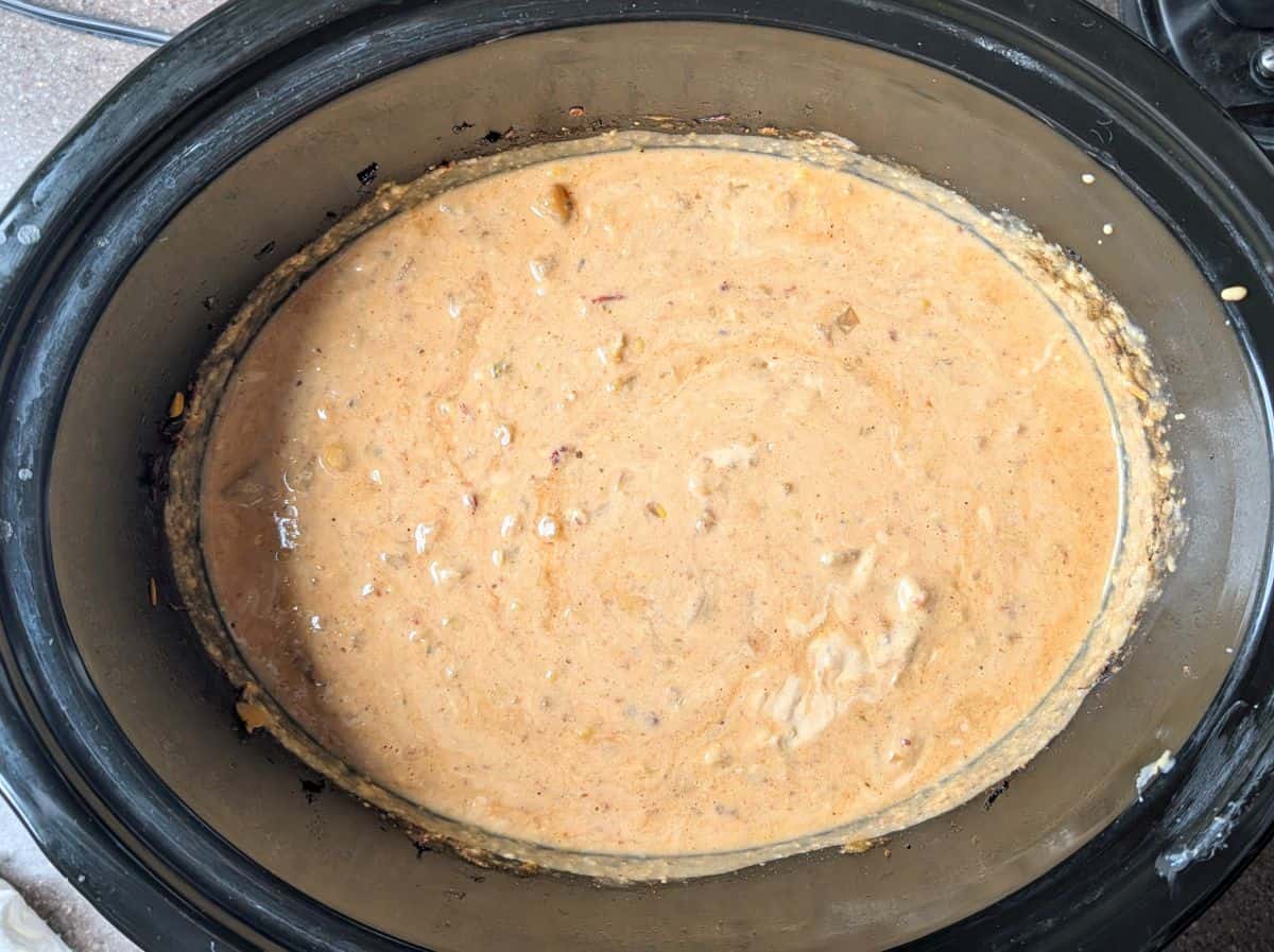 A top-down view of a slow cooker filled with creamy Mexican street corn soup after the blended cream cheese mixture has been stirred in.