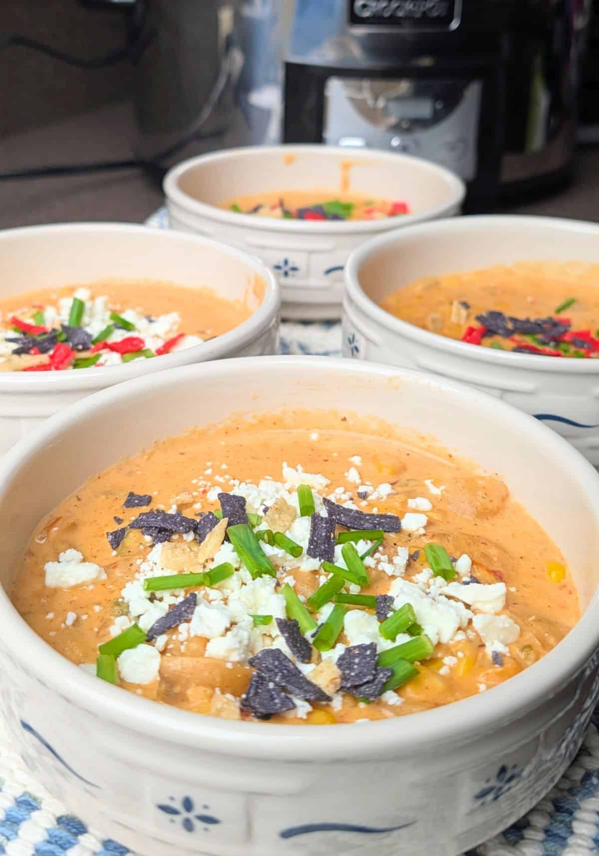 Four bowls of creamy Mexican street corn soup garnished with cotija cheese and fresh herbs, sitting on a kitchen counter ready to be served.