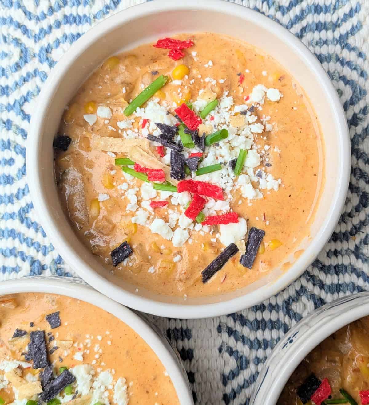 A top-down view of four bowls filled with creamy Mexican street corn soup, beautifully garnished with crumbled cotija cheese, fresh scallions, and tortilla strips.